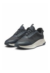 Dark grey athletic shoes feature a mesh upper, padded collar, textured accents, and a thick, contrasting white sole for traction.