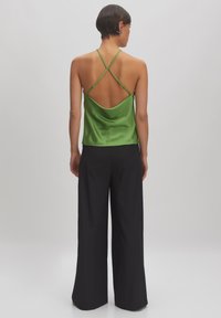 Groen satijnen cami-top met kruislings straps, met een open rugontwerp. Gepaarde met zwarte wijde broek. Soepele textuur.