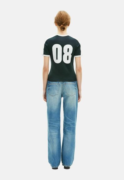 Grünes, kurzärmeliges T-Shirt mit weißen Akzenten und großer "08" auf dem Rücken, kombiniert mit hellblauen, locker sitzenden Jeans, beides lässig im Design.