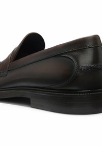 Mocassin en cuir noir avec finition lisse, bout arrondi, petit talon et coutures détaillées sur les côtés et à l’arrière.