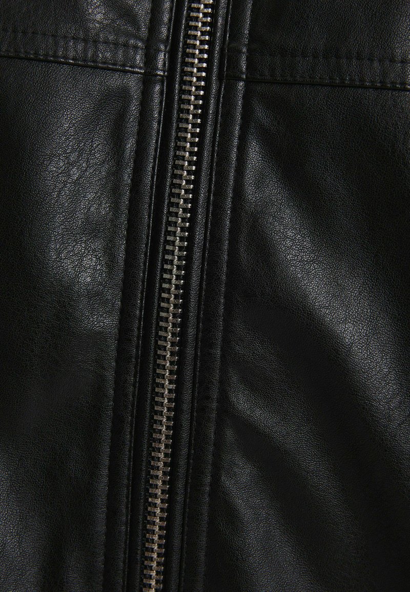 Chaqueta de cuero negra con un cierre central plateado, superficie ligeramente texturizada y costuras limpias a lo largo de las uniones.