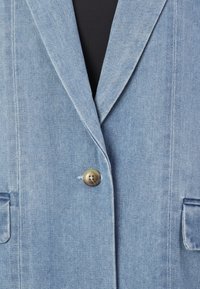 Svetlo modra denim jakna z ovratnikom s preklopom, enojnim zapiranjem z mesingastim gumbom in dvema sprednjima žepoma, z vidnim šivi in teksturo.