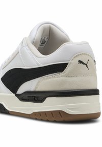 Hvide sneakers med en sort ruskindsstribe, tekstureret mesh-tunge, gummisål og Puma-logo på hælen. Glat læderoverdel.