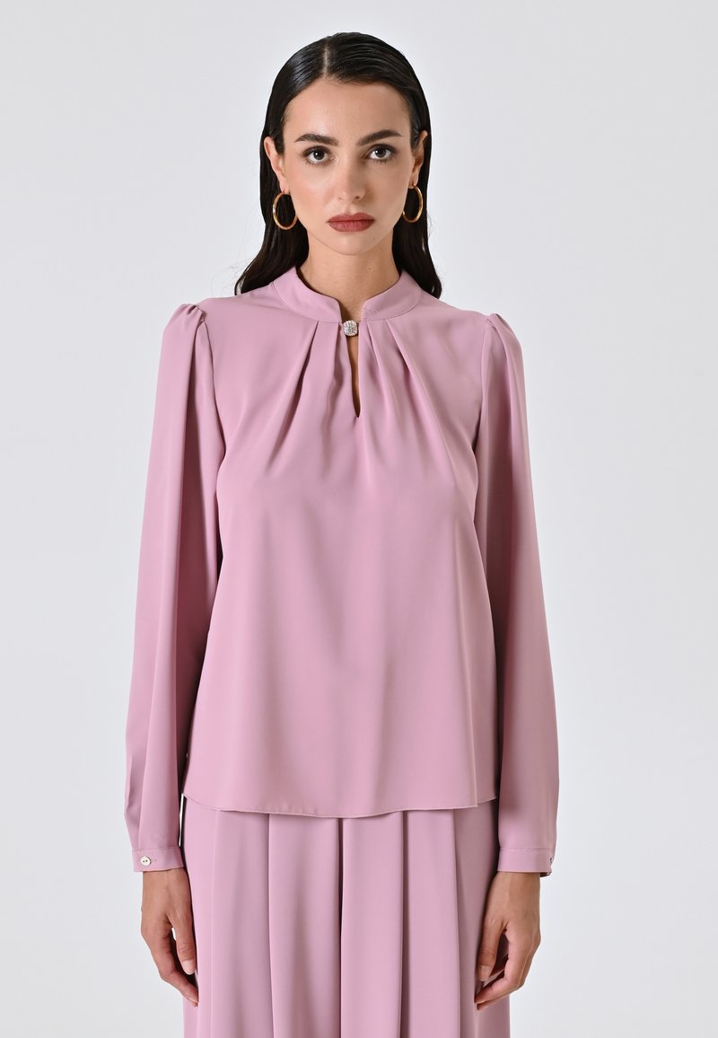 Blusa rosa pallido con scollatura a chiave, dettaglio plissettato sulle spalle, maniche lunghe e polsini abbottonati, realizzata in tessuto leggero.