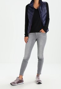 Granatowa puchowa kamizelka na czarnej bluzce, w połączeniu z szarymi obcisłymi jeansami i jasnoszarymi trampkami z ciemniejszymi akcentami. Proste, funkcjonalne ubranie.