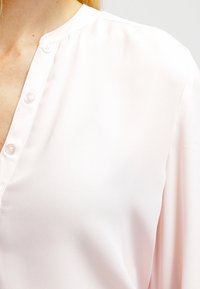 Rosa Bluse mit langen Ärmeln aus glattem Stoff und Kragen, mit einer Knopfleiste und sanft fallenden Ärmeln.