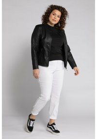 Zwarte leren jas, zwart topje, witte broek en zwarte sneakers. De jas heeft een rits sluiting en een gladde textuur, met nauwsluitende mouwen.