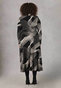 Vestito nero a maniche lunghe con linee bianche ondulate, aderente in vita, gonna fluida e scollatura rotonda. Indossato con stivaletti neri.