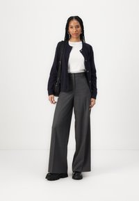 Námořnický svetr, bílý top, šedé pruhované široké kalhoty, černé robustní boty a malá černá kabelka přes rameno. Hladké textury, detaily knoflíků.