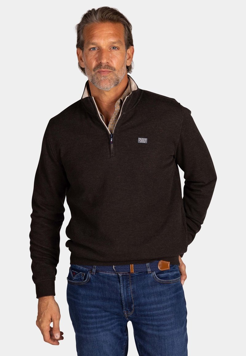Donkerbruine zip-up trui met een hoge kraag en logo op de borst, gecombineerd met blauwe jeans en een geweven riem. Gladde stoftextuur.