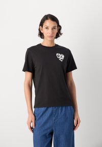 T-shirt nera in cotone con maniche corte, colletto rotondo e una grafica bianca a forma di cuore sul petto con dettagli facciali.