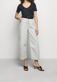 Woman wearing high-waisted wide-leg light gray pants, black belt, black short-sleeve v-neck top, and black heeled sandals.