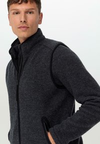 Dunkelgraue Weste mit hohem Kragen, durchgehendem Reißverschluss und schwarzen Akzenten. Hergestellt aus strukturiertem Fleece und ausgestattet mit seitlichen Taschen für Bequemlichkeit.