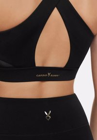 Black sports bra with cut-out design, featuring a logo in gold on the band and a small heart-shaped hardware accent on the waistband.