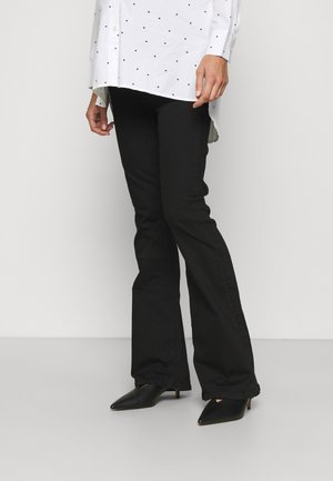 Calças flare pretas feitas de algodão. Apresenta uma textura suave, cintura ajustada e costuras subtis. Combinadas com uma camisa branca coberta de pequenos pontos pretos.