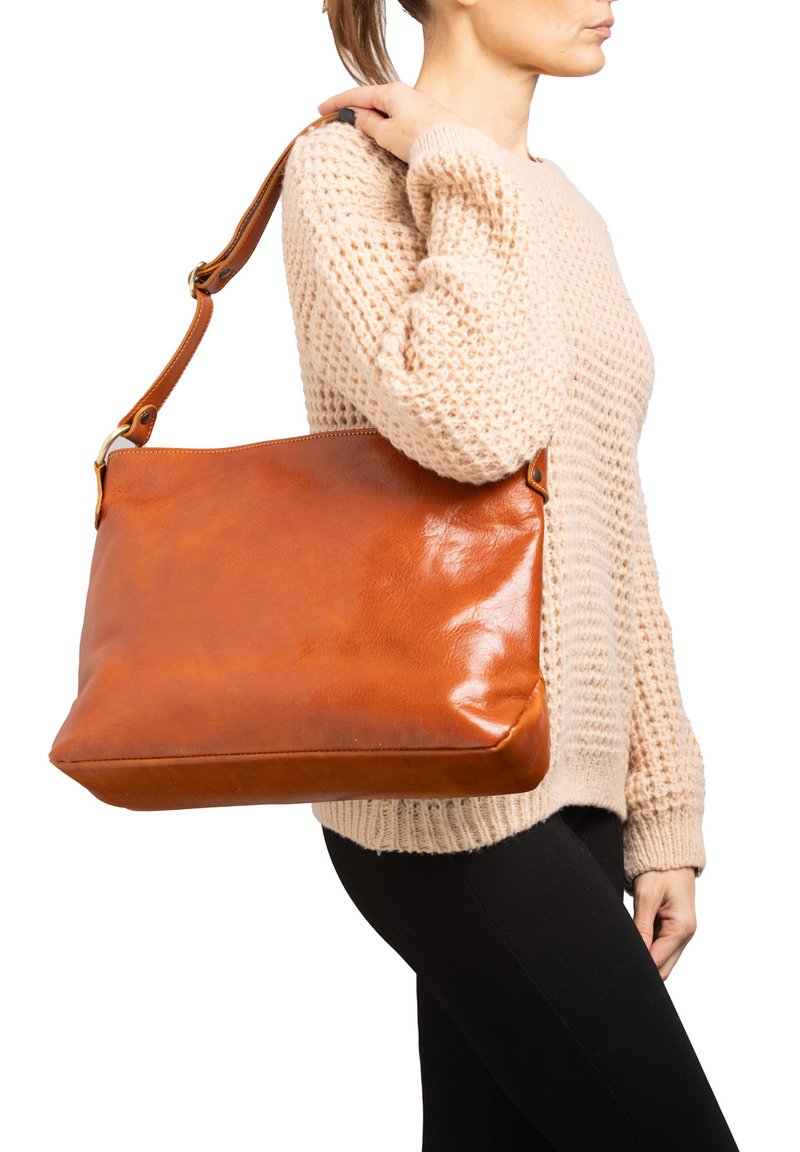 Donna con un maglione di maglia beige e pantaloni neri che porta una grande borsa a tracolla in pelle marrone sulla spalla destra.
