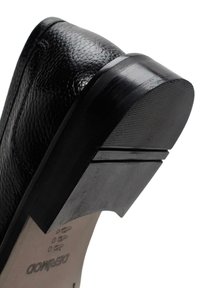 Zapato de cuero negro con un acabado texturizado, un tacón curvado y una suela de goma ancha que detalla ranuras verticales para mayor tracción.