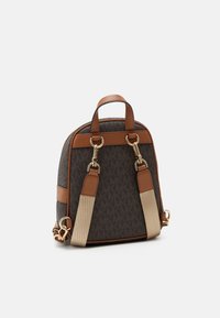 Kompaktní batoh z hnědé látky s monogramem, s akcenty z hnědé kůže, kováním se zlatým tónem, dvojími horními držadly a nastavitelnými popruhy.