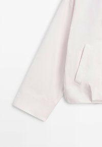 Long-sleeve light pink jacket sleeve with a wide cuff and a side welt pocket on a smooth fabric.