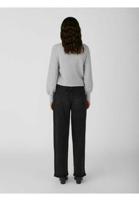 Grijze gebreide trui met ballonmouwen, gecombineerd met hoge zwarte spijkerbroeken, gezien van achteren. Zwarte schoenen maken de look af.