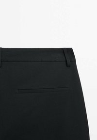 Czarne spodnie charakteryzujące się gładką teksturą, slim fit oraz jedną tylną kieszenią z wypustką. Zawierają szlufki na pasek w talii.