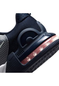 Sneaker blu navy con tomaia in mesh testurizzato, suola in gomma e ammortizzazione ad aria visibile nel tallone. Presenta un accento sul tallone arrotondato e un pannello grigio.
