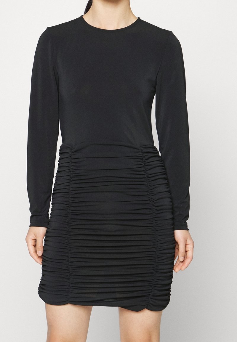 Svart långärmad klänning med rynkat design längs midjan och höfterna, med ett mjukt, stretchigt tyg för en figurnära siluett.
