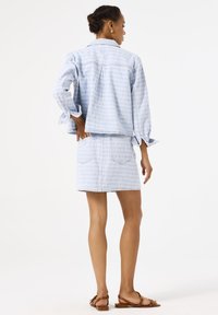 Chaqueta de denim azul claro con patrón texturizado, corte corto y mangas enrolladas, combinada con una falda de denim de talle alto a juego.