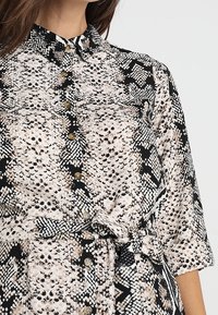 Abito camicia con un motivo a stampa serpente nero e beige, dotato di colletto, maniche a trequarti e vita legata per definire la silhouette.