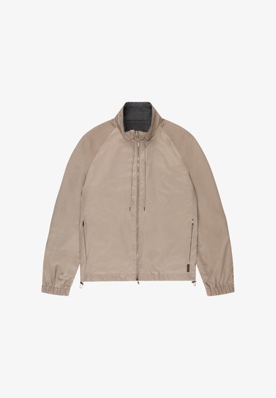 Giacca leggera beige con cerniera frontale, collo alto, coulisse, tasche laterali con cerniera e polsini elasticizzati, distesa su sfondo bianco.