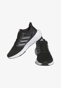 Scarpe da atletica nere con tomaia in rete, dettagli grigi e suola bianca. Presentano un design con allacciatura e tre strisce caratteristiche sui lati.