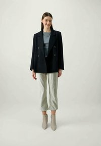 Double-breasted navy blazer with wide lapels, paired with a light gray top and cropped, light gray trousers. Beige ankle boots complete the look.
