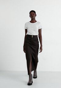 Tricou alb cu imprimeu leopard, asortat cu o fustă neagră cu talie înaltă, care are o fante și două nasturi pe față. Modelul poartă botine texturate până la gleznă.