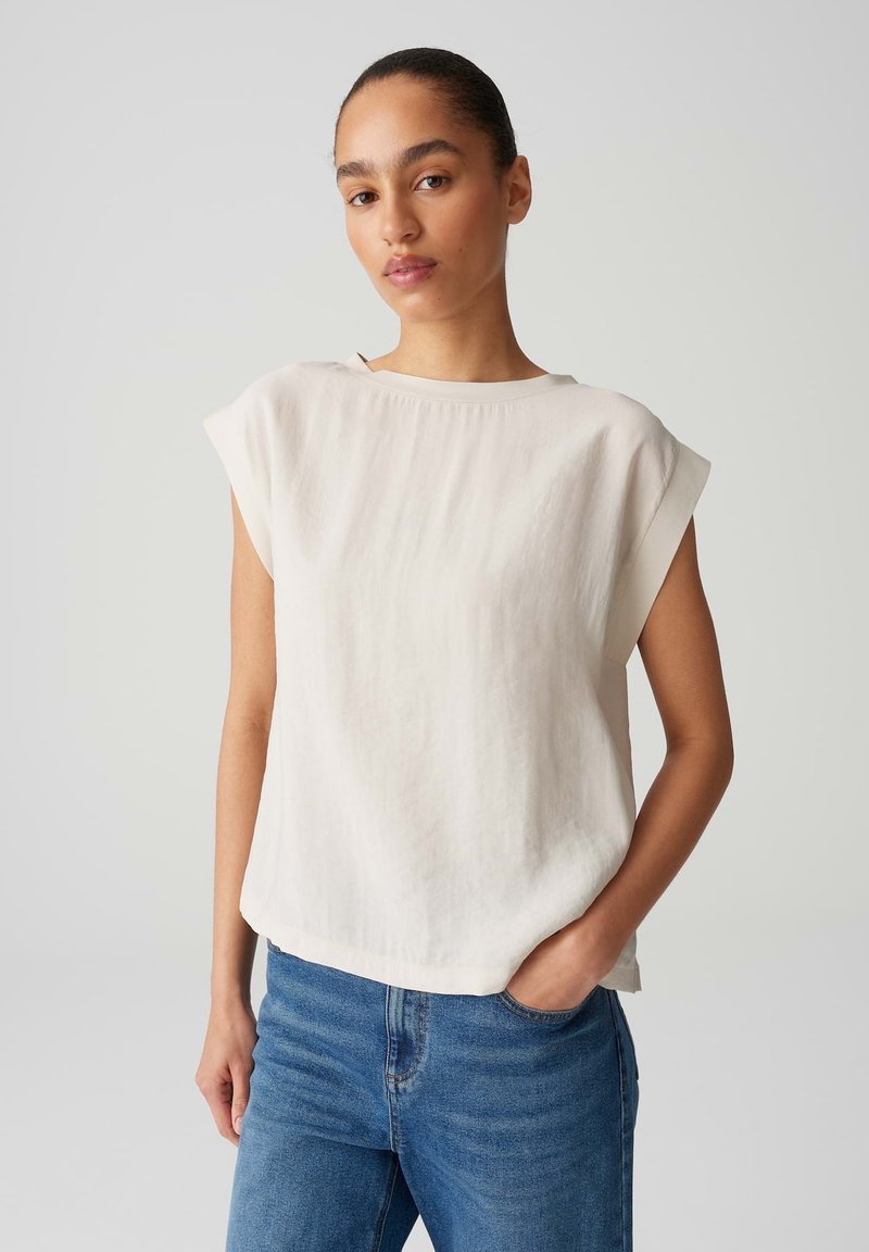 Cremfarbener Kurzarm-Oberteil mit Rundhalsausschnitt, aus leichtem Stoff, mit lockerem Schnitt und einem Saum, der leicht nach oben kurvt.