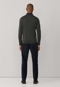 Grijze trui met een ronde kraag en lange mouwen, gecombineerd met donkerblauwe broek. De stof is glad met een getailleerd ontwerp.