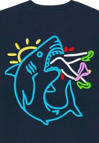 Tengerészkék póló színes, hímzett cápa mintával, napfénnyel, halakkal és növényekkel, kiemelve a vibráló fonalakat és a játékos ábrázolást.