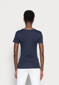 Camiseta de manga corta color azul marino con cuello redondo, diseño ajustado y textura suave. Combinada con pantalones blancos, con detalles mínimos.