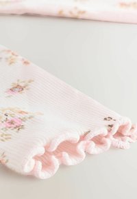 Tessuto a coste rosa chiaro con motivi floreali in tonalità di rosa e beige, caratterizzato da un bordo arricciato per un'ulteriore texture.