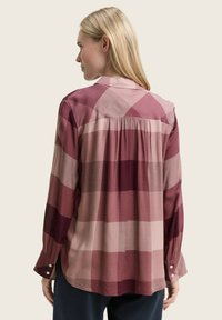 Chemise à manches longues dans des tons de rose et de bordeaux, arborant un motif à carreaux, des poignets boutonnés et un détail froncé dans le dos.