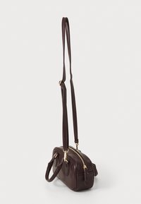 Dunkelbraune Lederhandtasche mit goldenem Reißverschluss, zwei kurzen Griffen und verstellbarem langen Schultergurt vor einem schlichten weißen Hintergrund.