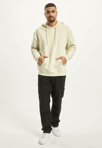 Lys beige hættetrøje med snoretræk, frontlommer, parret med sorte cargobukser og hvide sneakers. Blødt stof, afslappet pasform.