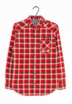 Rødt og hvidt ternet skjorte med knapper og brystlomme broderet med "G-STAR", hængende på en sort bøjle mod en hvid baggrund.