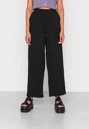 Woman wearing black wide-leg pants, black platform sandals, and a cropped purple sleeveless top with front zipper.