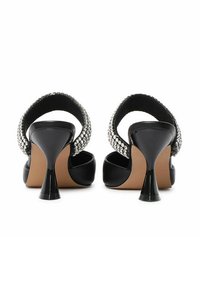 Zwarte hoge hak sandaaltjes met glanzende rhinestone accenten, open achterkant, gebogen banden en een taps toelopend hakontwerp. Gemaakt van soepel synthetisch materiaal.
