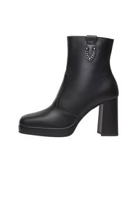 Schwarze Knöchelstiefelette aus glattem Leder, mit einem stabilen Blockabsatz, runder Zehenform und einem metallischen Ketten-Detail auf der Rückseite.