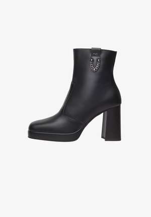 Zwarte enkelboot van glad leer, met een chunky blokhak, ronde neus en een metalen kettingdetail aan de achterkant.