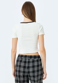 Hvid ribbet cropped t-shirt med en sort krave, parret med sort-hvide plaidbukser, der har elastisk talje og løst fit.