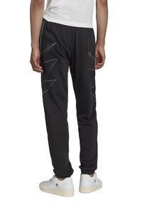 Černé tepláky se zigzagovým prošitím světle šedé barvy na zadní straně, vyrobené z měkkého materiálu, s elastickým pasem a zúženými manžetami.