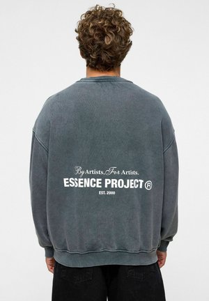Grijze oversized sweatshirt met een ronde hals, met op de achterkant witte tekst: "Door kunstenaars, Voor kunstenaars. ESSENCE PROJECT ® OPGERICHT. 2000."