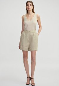 Shorts de lino beige claro con un corte relajado, que cuentan con una cinturilla elástica y un botón frontal, combinados con una blusa sin mangas a juego.